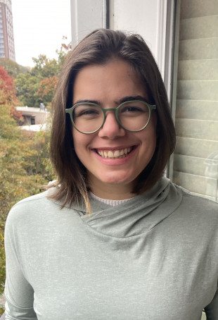 Ravyn smiling outside, wearing glasses and a light grey shirt.
