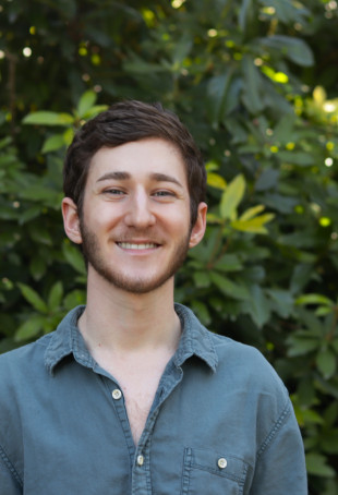 Avi posing outside wearing a blue button-up shirt.