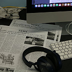 Photo of newspapers stacked up with headphones on top, near a computer.